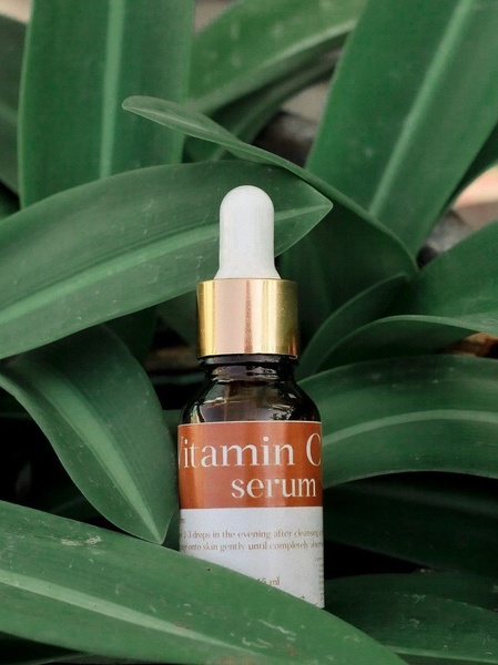 A high-quality product shot of a Vitamin C serum bottle nestled within lush green leaves, emphasizing purity and natural ingredients.